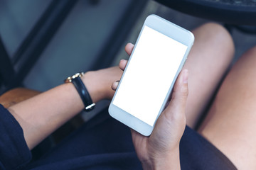 Mockup image of a woman sitting and holding white mobile phone with blank  desktop screen