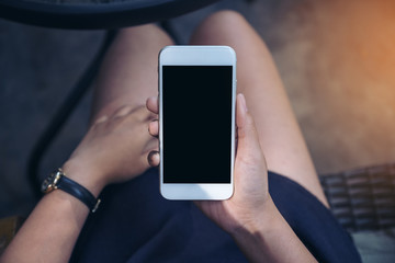 Top view mockup image of a woman sitting and holding white mobile phone with blank black desktop screen