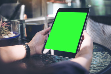 Mockup image of hands holding black tablet pc with blank white desktop screen and coffee cup on glass table