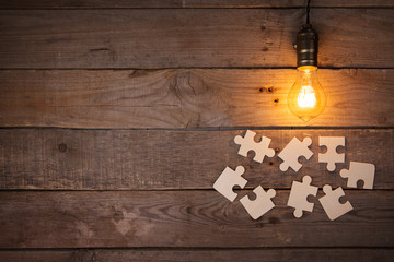 Retro light bulb and group of jigsaws on wooden background - idea, innovation, teamwork and...