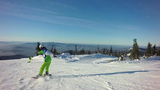 Snowboarder rides down the top of a mountain in sunny winter day
