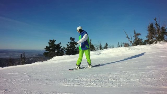 Snowboarder is riding down the peak of a mountain in sunny winter day