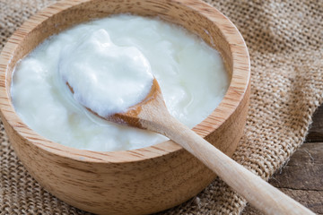 white natural homemade yogurt in wooden bowl with wooden spoon on gunny sack cloth on wood table, close up shot