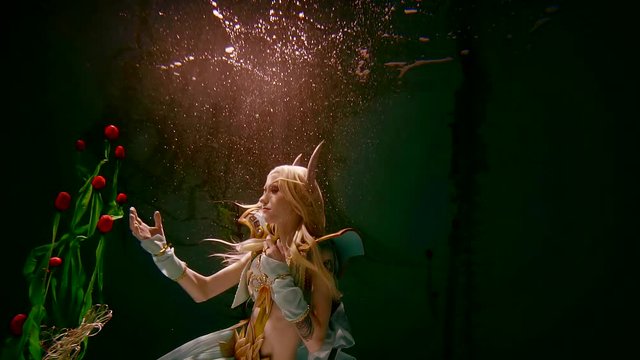 young girl in the elf costume is kept under water in the darkness illuminates the light. role play.