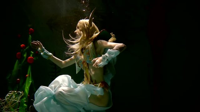 Slow motion. the girl in the armor and dress of the elf drifts under the water and touches the mysterious marine plants