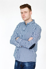 Fototapeta premium Cheerful handsome redhead young guy in black cardigan checkered shirt photographed against white wall in the studio