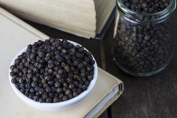 Pile black pepper on white bowl and glass jar on old wooden table.