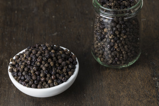 Pile black pepper on white bowl and glass jar on old wooden table.