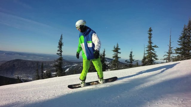 Man snowboarder is riding down the peak of a mountain in sunny winter day
