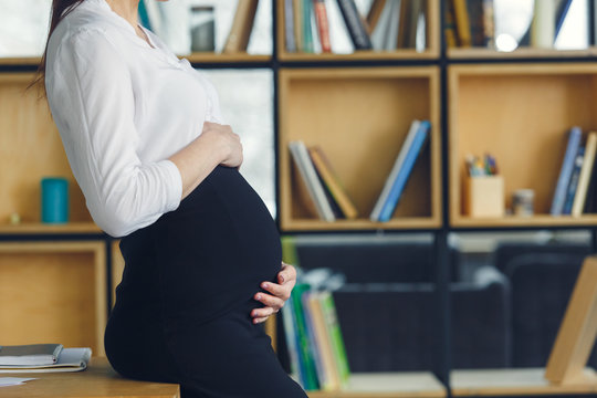 Pregnant business woman working at office motherhood touching belly