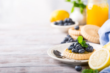 Shortbread homemade tartlet filled with lemon curd and fresh blueberries on rustic wooden background. Holiday food concept with copy space.