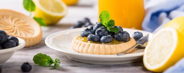 Shortbread homemade tartlet filled with lemon curd and fresh blueberries on rustic wooden background. Holiday food concept. Banner.