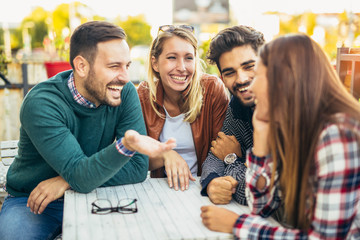 Group of four friends having fun a coffee together. Two women and two men at cafe talking laughing...