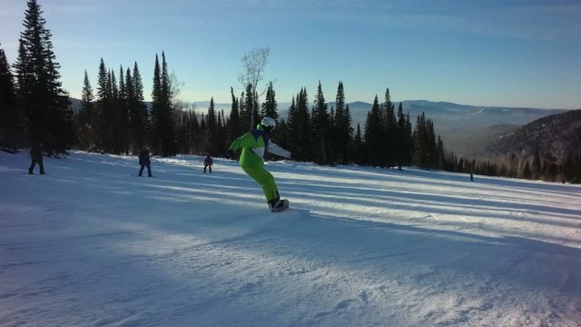 Man snowboarder rides fastly down the peak of a mountain in sunny winter day