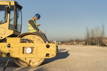  Construction worker looking smartphone on steamroller vehicle in rest