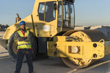 Bearded construction worker posing ner to steam roller machine