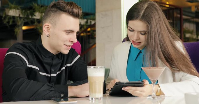 Couple in stylish suit talking in cafe, looking at tablet.