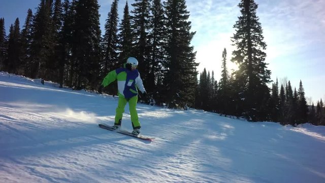 Man snowboarder is riding fastly down the peak of a mountain in sunny winter day