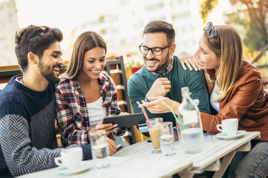 Group of four friends having fun a coffee together. Two women and two men at cafe talking laughing and enjoying their time