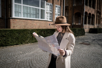 Young female tourist exploring map while standing in alley near vintage building. Trendy woman traveler with interest reading geographical atlas while touring in old city