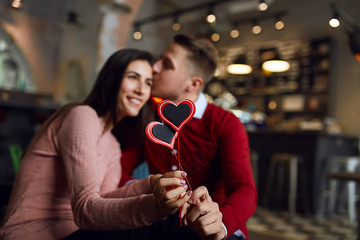 Beautiful couple celebrate Valentine's day in café, playing with toy hearts and enjoying each other.