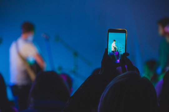 Rock Concert. Girl Is Taking Picture On Phone Camera At The Concert Of The Guitarist On Stage.