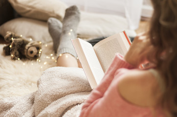 Coziness at home, girl doing hygge with book and warm blanket