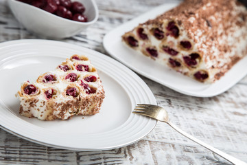 cake with cherries, cream and chocolate on a light wooden background