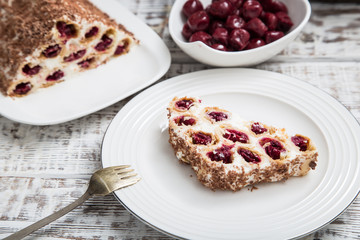 cake with cherries, cream and chocolate on a light wooden background