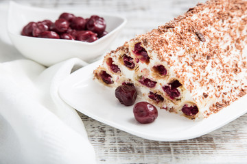 cake with cherries, cream and chocolate on a light wooden background