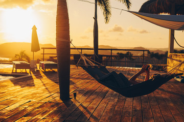 Frau genie&szlig;t beeindruckenden Sonnenuntergang in einer H&auml;ngematte