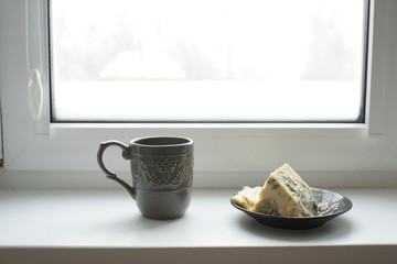 Mug with a drink and a plate of cheese dor blu at the window of a private house
