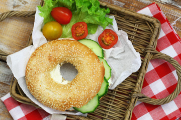 White sesame bagel with cream cheese and cucumber, cherry tomatoes on wicker tray

