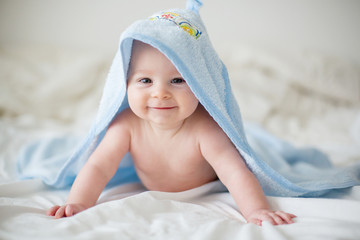 Cute little baby boy, relaxing in bed after bath, smiling happily