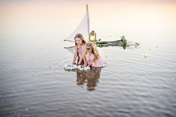 Girls in light dresses travel on a raft with a sail. The girls launch wreaths of white flowers.