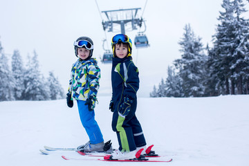 Cute little preschool children, boy brothers in blue jackets, skiing happily