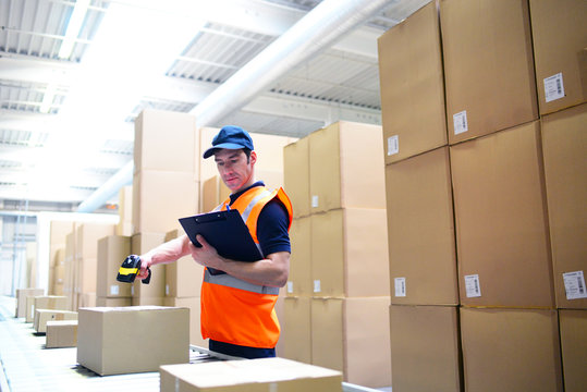Arbeiter im Versandhandel scannt Pakete am Fliessband zur Lieferung ein // Mail-order workers scan packages on conveyor belt for delivery