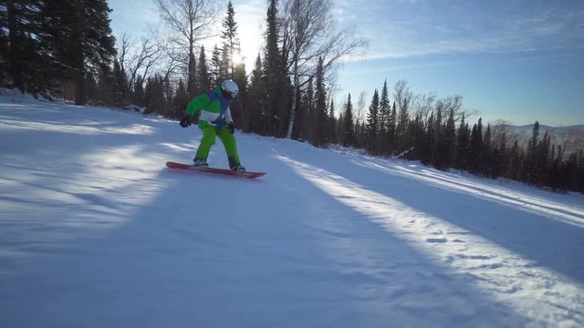 Sportsman snowboarder in bright clothes is riding down the top of a hill at winter sunny day