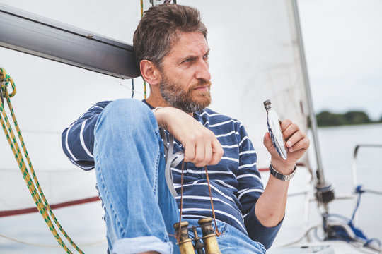 man with beard sits on deck of sailing yacht