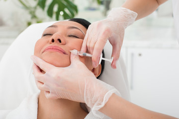 Strained asian woman taking an collagen injection in beauty salon. She is lying in a chair with closed eyes