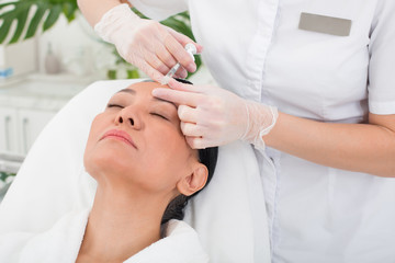 Obraz na płótnie Canvas Tense asian woman lying on the couch with closed eyes in beauty salon. Doctor is giving an injection to strained lady