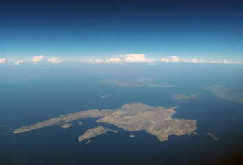 the island of kalymnos from the air with mainland in the distance with blue summer sky and band of white clouds on the horizon