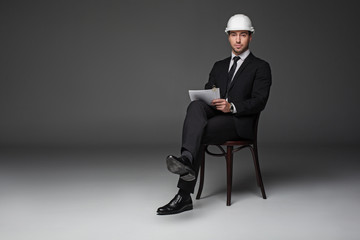 Full length portrait of serious architect working with paper while sitting at chair. Job concept. Copy space