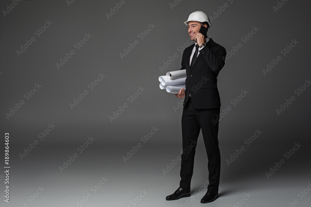 Aufkleber full length side view cheerful unshaven builder speaking by mobile while holding projects in arm. co