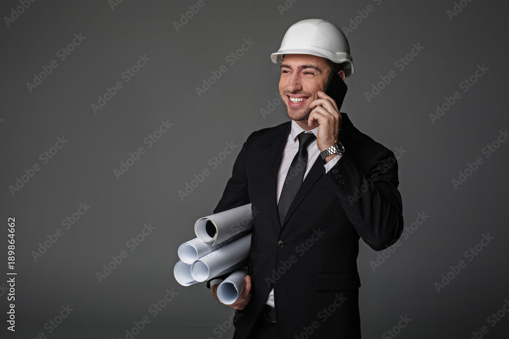 Aufkleber portrait of cheerful unshaven builder telling by mobile while keeping different projects in hand. co