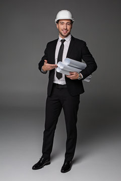 Full length portrait of beaming bearded master-builder pointing at plans by arm. Labor concept