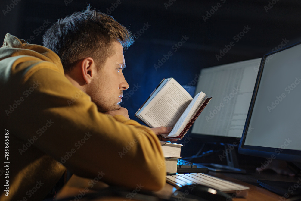 Poster side view calm unshaven man reading interesting text while sitting at desk near digital device. educ