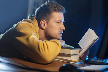 Side view serene unshaven man reading interesting volume while sitting at desk. Education concept
