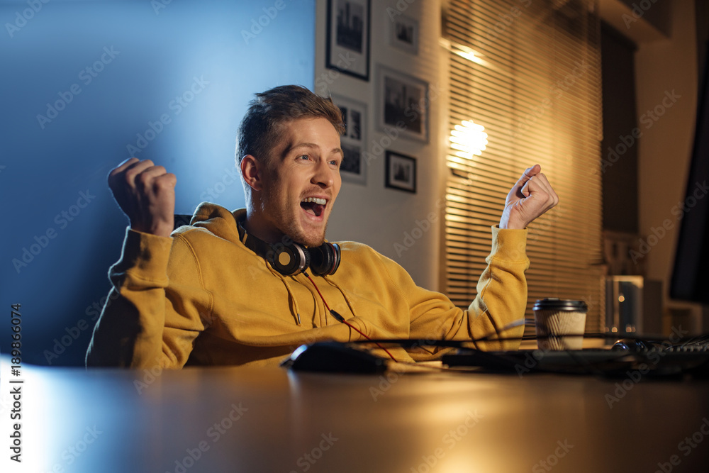 Poster portrait of happy man gesturing hands while sitting at table. he looking at computer. win concept