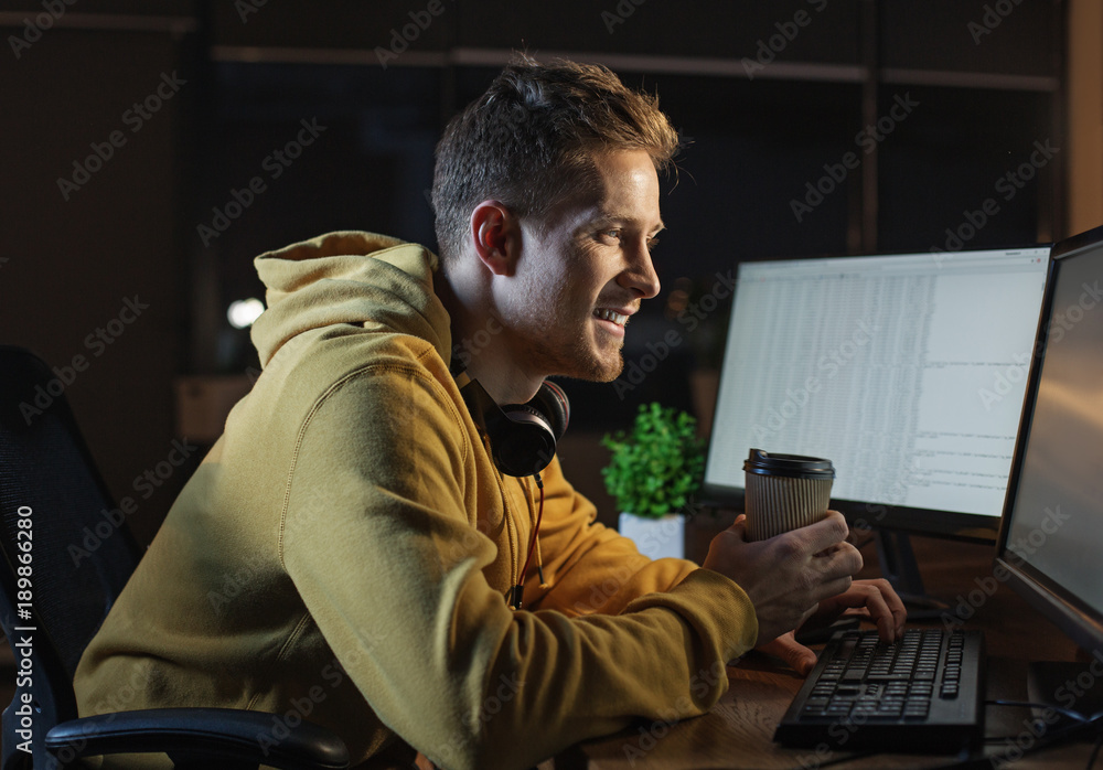 Poster side view cheerful bearded man drinking cup of coffee while typing in keypad of modern digital devic